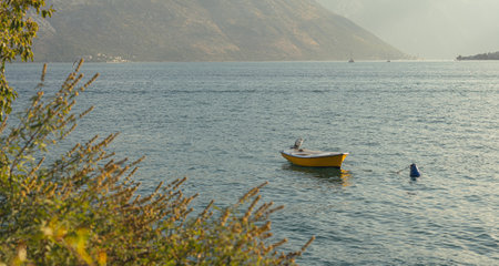 Lonely Yellow Boat Drifting Peacefully on a Calm Lake with Mountain Viewsの写真素材