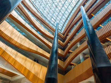 A stunning view of a modern atrium with tall pillars, layered wooden balconies, and a glass ceiling, showcasing contemporary architectural elegance.の写真素材