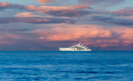 A luxurious yacht sails across the calm ocean under a stunning, colorful sunset sky, capturing a moment of tranquility and elegance.の写真素材