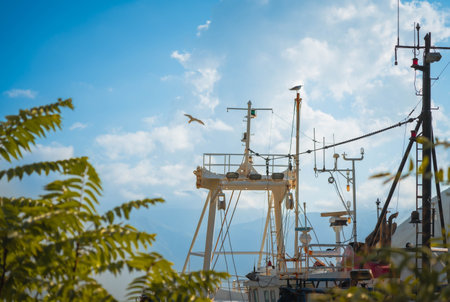 A fishing boats mast and antennas rise against a clear blue sky with seagulls soaring, creating a peaceful maritime scene.の写真素材