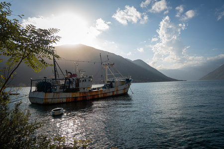 The rustic charm of a fishing boat by the shore with majestic mountains in the background under a serene evening sky.の写真素材