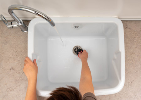 A close-up view of a person cleaning a utility sink with running water from a faucet.の写真素材