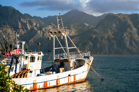 A weathered fishing boat anchored by the coast with rugged mountains in the background, capturing the essence of a peaceful maritime landscape.の写真素材