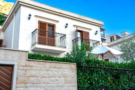 A modern villa with balconies and a lush garden surrounded by a stone fence, emphasizing elegance and outdoor living.の写真素材