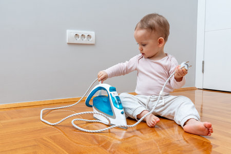 A curious toddler exploring an iron cord, creating a potential safety hazard with an electrical outlet nearby.の写真素材