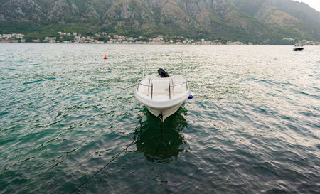 A small motorboat moored in calm bay waters with a picturesque mountain backdrop and serene coastal villages in the distance.の写真素材