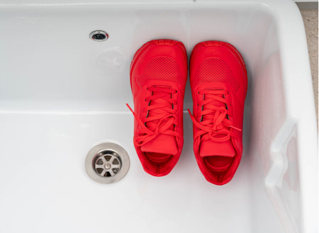 A pair of vibrant red sneakers placed inside a white sink, ready for cleaning and freshening up.の写真素材