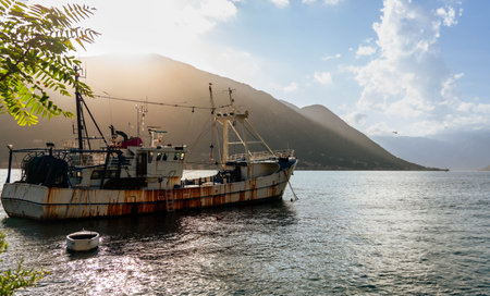 A tranquil coastal scene with a weathered boat anchored near mountainous shores, capturing the beauty of a peaceful sunsetの写真素材