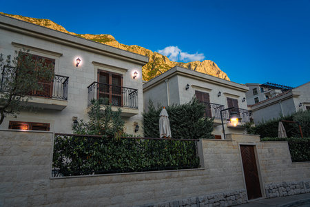 Elegant Mediterranean-style villas with balconies and lush gardens, nestled at the base of mountains under the evening sky.の写真素材