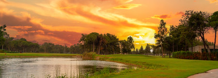 A glowing sunset over a tranquil golf course with a serene pond, vibrant skies, and lush greenery, offering a peaceful retreat.の写真素材
