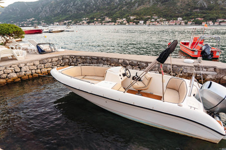 A sleek white motorboat docked at a scenic bay, surrounded by mountains and a charming waterfront setting, ready for adventure.の写真素材