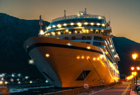 A majestic cruise ship illuminated at night, docked at a tranquil harbor under a twilight sky, symbolizing luxury and adventure.の写真素材