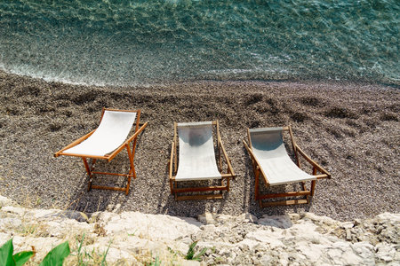 Three lounge chairs on a serene pebble beach by the water, offering a tranquil spot for relaxation...