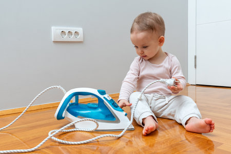 Toddler innocently playing with an iron plug, unaware of potential danger.の写真素材