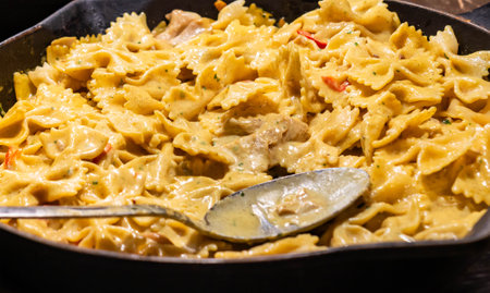 A creamy farfalle pasta dish with tender meat and vegetables, cooked to perfection in a rich cheese sauce, served hot in a skillet.の写真素材
