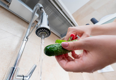 Washing and peeling a fresh cucumber under running water, emphasizing cleanliness and preparation for a healthy meal.の写真素材