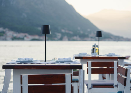 Romantic waterfront dining with elegant table settings, overlooking serene mountains and a tranquil bay at sunset.の写真素材