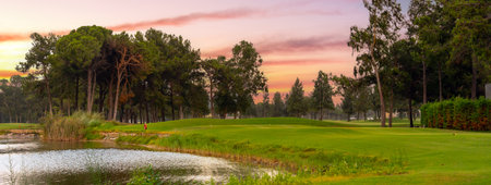 A tranquil golf course with a reflective pond and lush greenery, set against the soft pastel hues of a peaceful sunset.の写真素材