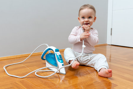 A curious toddler playing with an iron plug and cord, highlighting the risks of electrical outlets in homes with small children.の写真素材