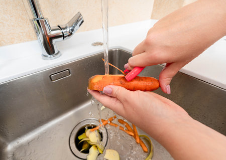 Peeling a fresh carrot under running water with waste collected in a garbage disposer.の写真素材