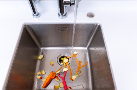 Kitchen sink with running water and vegetable peels during cleanup.の写真素材