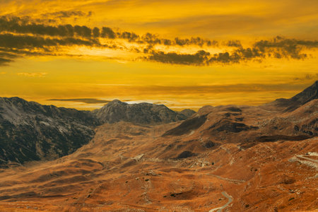 Golden sunset over a majestic mountain landscape with dramatic sky and rocky terrain.の写真素材