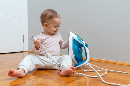 Exploring toddler holding iron cord close to a power outlet, highlighting household safety concerns.の写真素材