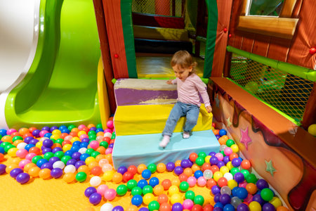 A cheerful indoor playground with a child playing near a colorful ball pit and slide.の写真素材