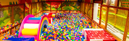 Panoramic view of a colorful indoor ball pit with rainbow slide and soft blocks for kids.の写真素材