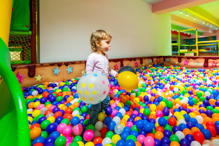 A cheerful child with balloons exploring a colorful ball pit in a lively indoor playground.の写真素材