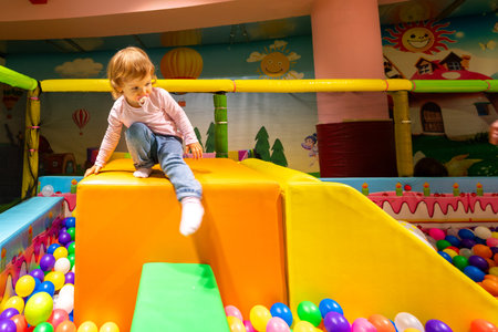 A playful child climbing a soft slide in a colorful ball pit at a vibrant indoor playground.の写真素材