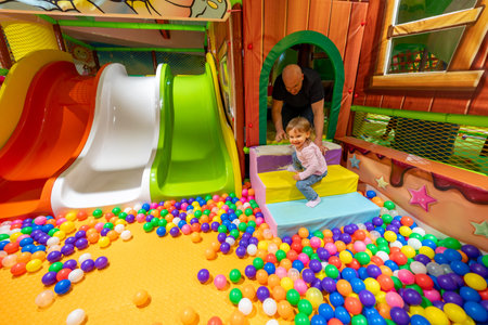 A colorful indoor playground with a ball pit, slides, and a child playing under adult supervision.の写真素材
