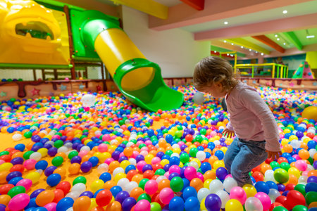 A happy child playing in a colorful ball pit with a green slide in the background.の写真素材
