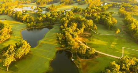 A panoramic aerial view of a golf course with ponds and lush greenery illuminated by golden sunlightの写真素材