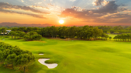 A golden sunset view of a golf course with sand traps and vibrant greeneryの写真素材