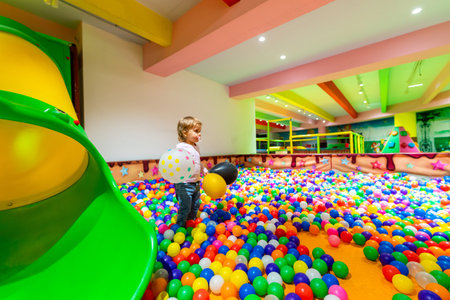 A child holding balloons surrounded by colorful balls in a vibrant indoor playground.の写真素材