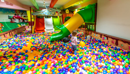 A joyful child with balloons exploring a vibrant ball pit near playground slides.の写真素材