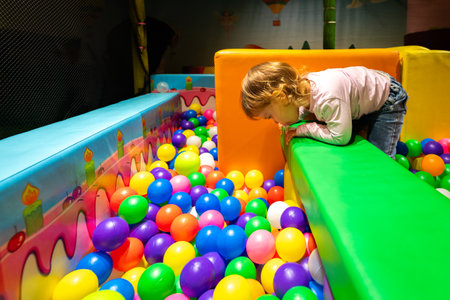 A curious child leaning over a soft structure observing colorful balls in a vibrant play area.の写真素材