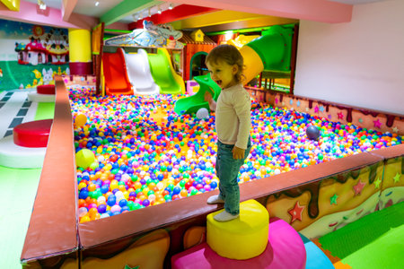 A child standing confidently on a soft play structure near a colorful ball pit in a lively playground.の写真素材