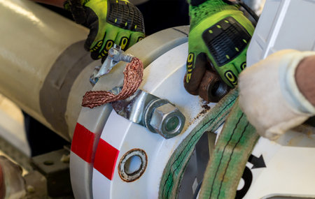 Workers dismantling a flanged pipeline connection using lifting straps and gloves.