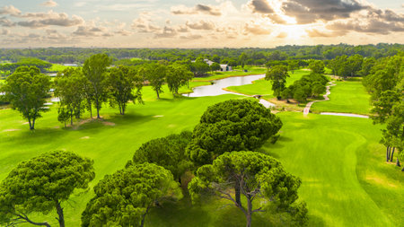Panoramic view of a golf course with a winding river, lush greenery, and a cloudy skyの写真素材
