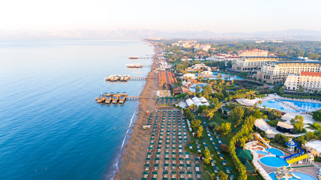 Aerial view of a luxurious beachfront resort with private piers, pools, and sunbeds along the coastlineの写真素材