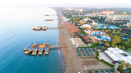 Aerial view of a luxury beachfront resort with floating bungalows, private piers, and a sandy coastlineの写真素材