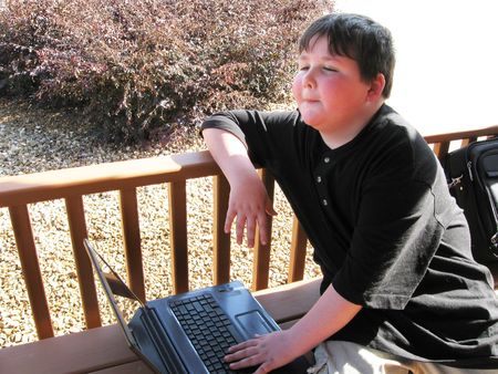 Young boy working on laptop outside in the sunの写真素材