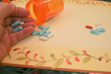 Hand holding pills with empty bottle on tableの写真素材