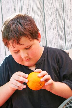 Boy peeling a ripe orangeの写真素材