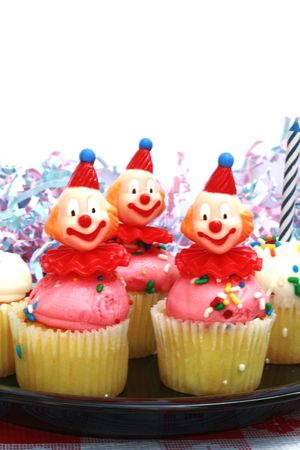 Three cupcakes with frosting, candles and clown headsの写真素材