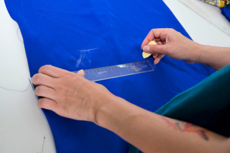 female dressmaker drawing line on blue fabric on table close-up