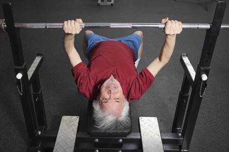 Senior man in gym working out with weights, bench pressing.の写真素材