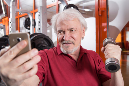 Elderly man taking a selfie with smartphone in fitness center